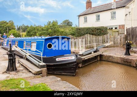 Schmalboot, das durch die Doppeltreppenschleusen auf dem Shropshire Union Kanal bei Bunbury Cheshire fährt, mit Blick auf das Schleusenhäuschen Stockfoto