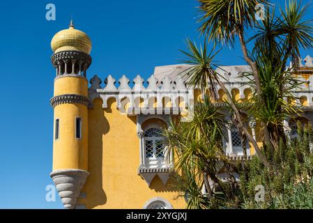 Pena-Palast-Außenarchitektur Sintra Portugal | SINTRA, Portugal — Die lebendige Fassade des Pena-Palastes mit seiner markanten gelben Außenhülle und Kuppel ist einer der bekanntesten Ausdrücke der romantischen Architektur des 19. Jahrhunderts in Europa. Ferdinand II ließ den älteren Klosterblock tiefrot und den neuen Palastflügel leuchtend gelb streichen, sodass das Gebäude wie eine farbenfrohe Krone vor dem Grün der Serra wirkt — ein Farbschema, das in einer Restaurierungskampagne von Parques de Sintra wiederhergestellt wurde, nachdem die Anstriche im Laufe des 20. Jahrhunderts zu Grau verblichen waren. Der Bau ging von ungefähr Stockfoto