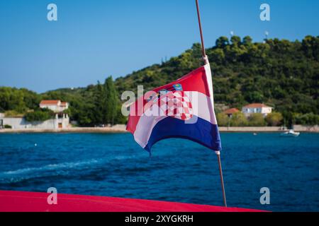 Kroatische Flagge winkt im Wind auf einem Segelboot mit Insel im Hintergrund. Stockfoto