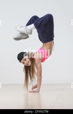 Fröhliche Hip-Hop-Tänzerin aus Preteen, die Handstand auf grauem Hintergrund macht Stockfoto