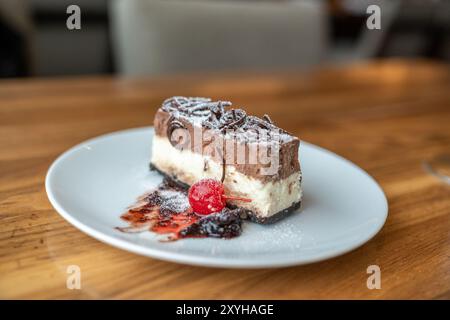 Ein Stück Schokoladenmousse Käsekuchen Dessert und eine Kirsche auf einem weißen Teller mit Kopierraum Stockfoto