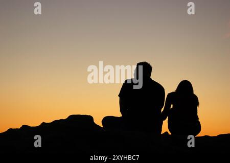 Ein junges Paar beobachtet den Sonnenuntergang, während es auf einem Felsen am Ufer sitzt und einen romantischen Urlaub in Laguna Beach, Kalifornien, macht Stockfoto