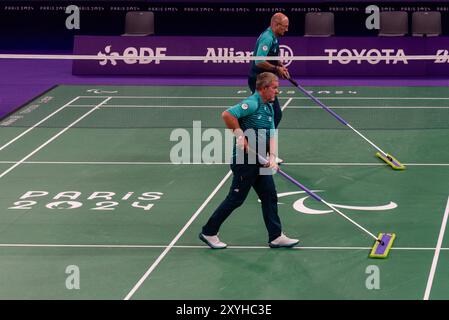 Paris, Frankreich. August 2024. Zwei Freiwillige reinigen den Boden des Badminton-Platzes während der Para Badminton Mixed Doubles SL3-SU5 Group Play Stage am ersten Tag der Paralympischen Spiele 2024 in der Arena Porte de La Chapelle. Quelle: Fabienne Koch/Alamy Live News Stockfoto