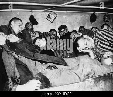 Überlebende in Dachau packten sich in überfüllte Schlafplätze, in denen sich sieben Männer zwei kleine Betten teilen mussten. Dachau war das erste Konzentrationslager der nazis, das am 22. März 1933 eröffnet wurde (nur sieben Wochen nach der Machtergreifung Hitlers). Obwohl es ein Zwangsarbeitslager war und es dort keine Gaskammern gab, waren Brutalität und gewalttätige Strafen die Norm. Dort gab es 32000 dokumentierte Todesfälle und viele Tausende weitere undokumentierte Todesfälle. Das Hauptlager (Dachau hatte 100 Unterlager) wurde am 29. April 1945 von der US-Armee befreit. Stockfoto