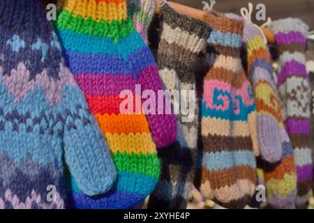 Mehrere handgefertigte Handschuhe aus gehäkelter Wolle in leuchtenden Farben hängen in einer Linie. Stockfoto