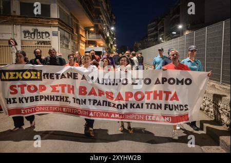 Athen, Griechenland. August 2024. Demonstranten marschieren mit einem Banner mit der Aufschrift „stoppt die Grausamkeit der Regierung der Banken und der Fonds“ während eines Protests gegen eine Vertreibung der Familie aus ihrem Haus aufgrund von Zwangsvollstreckungen. Die Demonstranten beschuldigen die Banken, die Gelder und die griechische Regierung für Grausamkeit, da sie behaupten, dass die Familie, die ihre Hypothek nicht zurückzahlen kann, ein behindertes Kind habe. Das Land steht vor einem sich verschärfenden Wohnungsmangel, der zu einem ernsten sozialen Problem geworden ist und für normale Haushalte äußerst unerschwinglich ist. Quelle: Dimitris Aspiotis/Alamy Live News Stockfoto