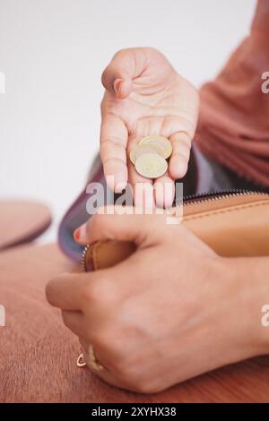 Nahaufnahme einer weiblichen Hand, die Münzen in der Nähe einer offenen Brieftasche auf einem Holztisch hält Stockfoto