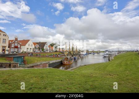 Blick auf historische Häuser mit bunten Fassaden am alten Hafen von Greetsiel, mit Fischerboot, unter blauem Himmel, Greetsiel, Ostfriesland, Niedersachsen Stockfoto