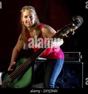 Musiker mit rotem Hemd spielt einen Kontrabass vor schwarzem Hintergrund Stockfoto