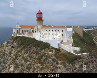 Ein roter Leuchtturm und weiße Gebäude stehen auf einer Klippe, umgeben von Vegetation und dem Meer, aus der Vogelperspektive, Leuchtturm, Cabo de Sao Vicente, Kap St. V. Stockfoto