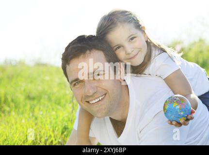 Glücklicher junger Vater mit einer kleinen Tochter draußen, die den Globus hält Stockfoto