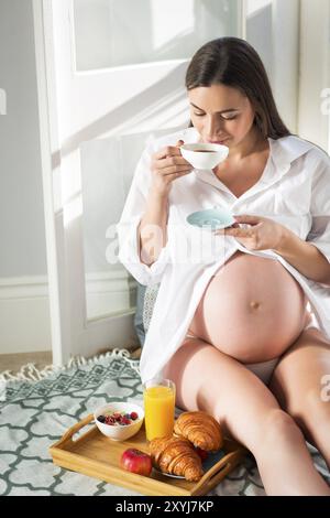 Schwangere Frau beim Frühstück mit Kaffee, Orangensaft, Croisan und Haferbrei Stockfoto