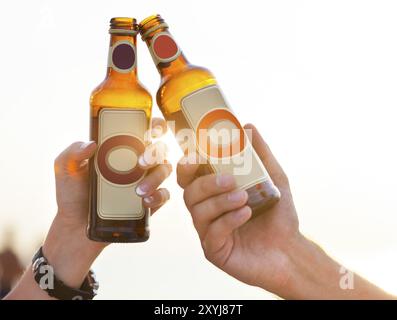 Paare am Strand feiern, trinken und Spaß im Sonnenuntergang haben, Flaschen in den Händen halten, während die Sonne durchscheint Stockfoto