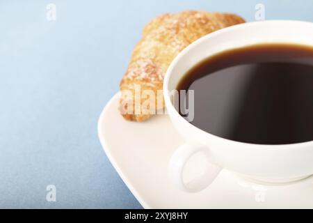 Kaffee und ein Croissant auf blauem Hintergrund Stockfoto