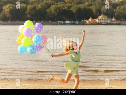 Glückliche Frau am Strand mit farbigen Tupfen Ballons springen Stockfoto