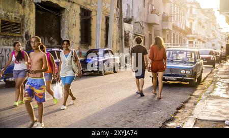 Havanna, Kuba am 22. Dezember 2015: Kubanische Menschen gehen in einer Straße im alten Havanna bei Sonnenuntergang. Am Straßenrand gibt es viele Oldtimer Stockfoto