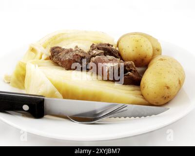 Hammelfleisch mit Kohl, Messer und Gabel auf weißer Platte zu weißem Hintergrund Stockfoto