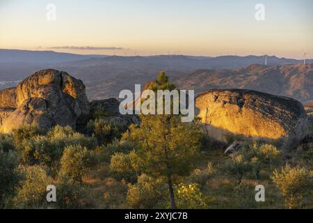 Sortelha Naturlandschaft Blick mit Bergen, Bäumen, Felsbrocken und Windturbinen bei Sonnenuntergang, in Portugal Stockfoto