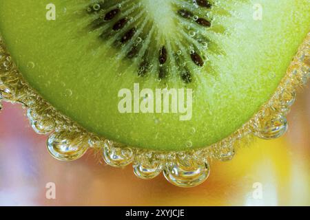 Kiwi im Wasser mit Luftperlen vor farbenfrohem Hintergrund Stockfoto