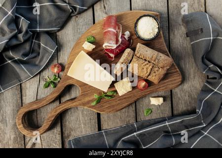 Italienische Küche Konzept flach Lay. Schneidebrett, Parmesan-Käsestückchen, geriebener Käse in schwarzer Schüssel, dünn geschnittener Schinken, Kirschtomate, Basilikumblätter b Stockfoto