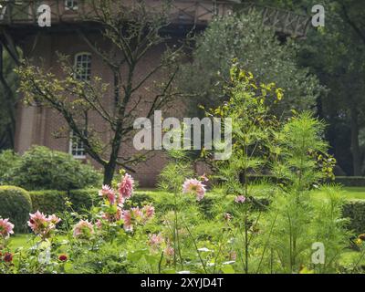 Blühender Garten vor einer großen Windmühle, umgeben von Bäumen und gepflegten Pflanzen, Bad Zwischenahn, ammerland, deutschland Stockfoto