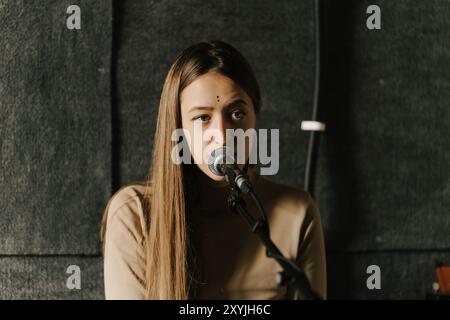 Junge Frau, die im Aufnahmestudio ins Mikrofon singt und in ihrer Aufführung Fokus und Leidenschaft vermittelt. Stockfoto