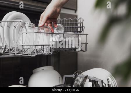 Nahaufnahme der weiblichen Hand, die in eine offene, automatische, integrierte Geschirrspülmaschine mit sauberen Utensilien geküst, entleeren oder entladen wird Stockfoto