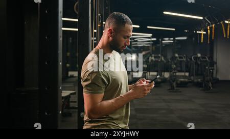 Amerikanischer Latino ethnischer Mann, der Smartphone surft ernsthaft Athlet fit Sport Guy Personal Fitness Trainer Trainer männlich in Gym Bodybuilder Sportler Stockfoto