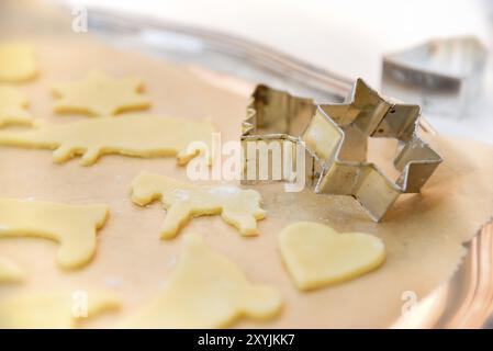 Weihnachtsgebäck, die vor dem Backen mit Keksschneidern in traditioneller Form ausgeschnitten werden. Auf einem antiken silbernen Tablett mit Backpapier. Teig für Stockfoto