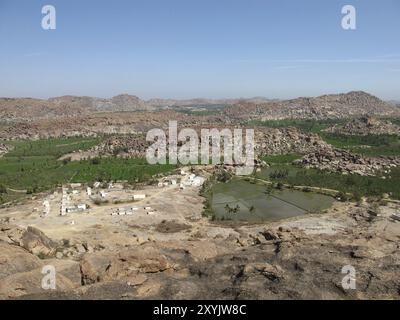 Kleines Dorf in der Nähe von Hampi, Indien. Reisfelder und Granitberge Stockfoto