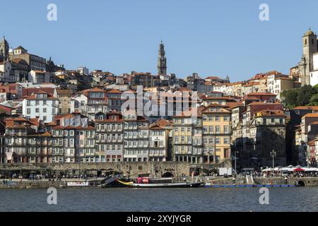 Historische Fassaden von Geschäften und Restaurants an der Promenade Cais da Ribeira am Fluss Douro und der Kirchturm Torre dos Clerigos in der Altstadt Stockfoto