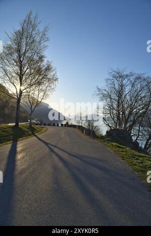 Parkplatz mit Blick auf die Straße, den Nordfjord und Bergen in Norwegen. Sonnenstrahlen fallen durch die Bäume. Landschaftsaufnahmen aus Skandinavien Stockfoto