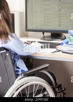 Ungültige oder behinderte junge geschäftsfrau sitzende Person Rollstuhl arbeiten Büro Schreibtisch computer Stockfoto