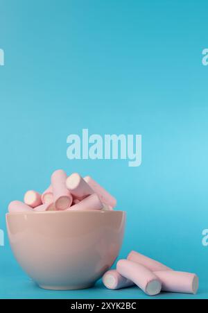 Ein detailliertes, vertikales Bild mit einer rosafarbenen Schüssel voller weicher Marshmallows, begleitet von einem kleinen Stapel Marshmallows auf der linken Seite. Das helle Stockfoto