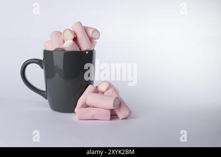 Ein grauer Becher mit Marshmallows befindet sich auf der linken Seite des Bildes, mit einem kleinen Haufen Marshmallows daneben. Die Szene ist gegen eine Sauberkeit gerichtet Stockfoto