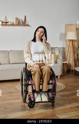 Eine Frau im Rollstuhl benutzt ihr Handy, während sie in ihrem Wohnzimmer sitzt. Stockfoto