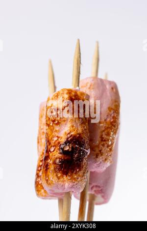 Detaillierte Ansicht der Spieße mit gerösteten Marshmallows, vertikal auf weißem Hintergrund angeordnet. Die Marshmallows sind gleichmäßig gebräunt, was ihre hervorhebt Stockfoto