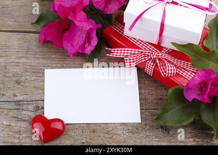 Geschenk-Boxen, rosa Bougainvillea, Herzen und Notizblock auf Holzbrett Stockfoto