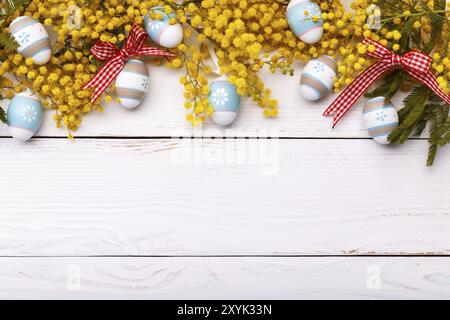 Ostern Hintergrund mit bunten Eiern und Mimosa Blumen auf weißem Holzbrett Stockfoto