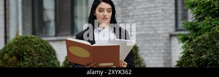 Eine Frau im Rollstuhl liest ein Buch, während sie vor einem Gebäude sitzt. Stockfoto