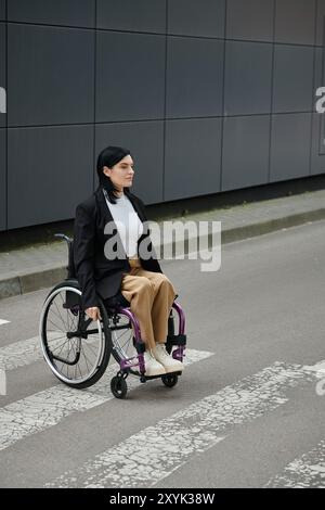 Eine Frau im Rollstuhl überquert eine Straße vor einem Gebäude. Stockfoto