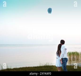 Junges Paar starten eine grüne chinesische Himmelslaterne in der Abenddämmerung am Meer Stockfoto