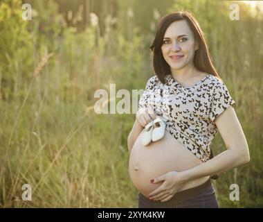 Schwangere Frau mit Baby Schuhe etwas auf ihrem Bauch bei Sonnenaufgang Hintergrund Stockfoto