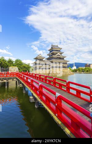 Schöne rote Holzbrücke führt über den Graben, um Wasser zu den von Matsumoto Schloss an einem sonnigen Sommertag in Nagano, Präfektur, Japan halten. Vertikale Stockfoto