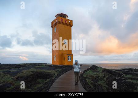 Frau, die vor dem orangefarbenen Leuchtturm in Island steht Stockfoto
