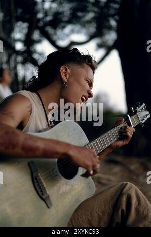 Ein junger Mann spielt Gitarre im Park bei Sonnenuntergang. Stockfoto