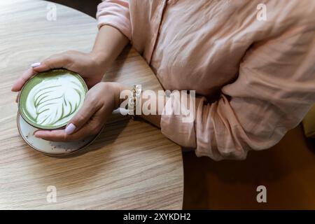 Eine Frau hält eine Tasse Matcha Latte und Latte Art in den Händen Stockfoto