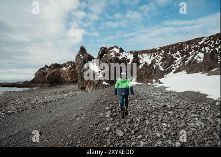 Junge erkunden Sie den schneebedeckten, felsigen schwarzen Strand Djúpalónssandur Island. Stockfoto