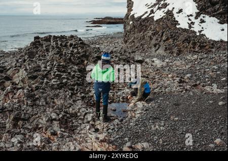 Zwei Brüder erkunden den schneebedeckten schwarzen Strand von Djúpalónssandur in Island Stockfoto