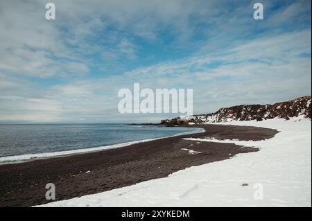 Schneebedeckter schwarzer Strand Djúpalónssandur Meer und blauer Himmel in Island. Stockfoto